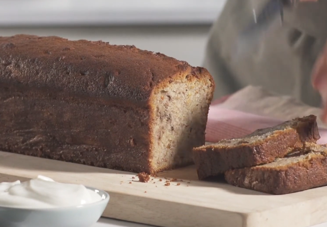 "Freshly baked Fage banana bread loaf sliced on a wooden cutting board."